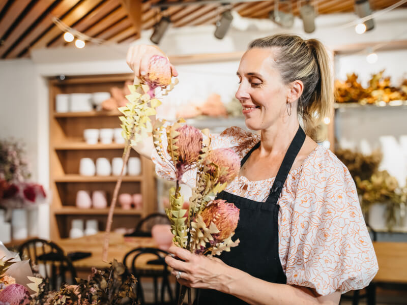A picture of a woman smiling as she holds flowers in a floristry class.